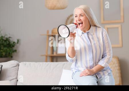 Screaming mature woman with megaphone at home Stock Photo