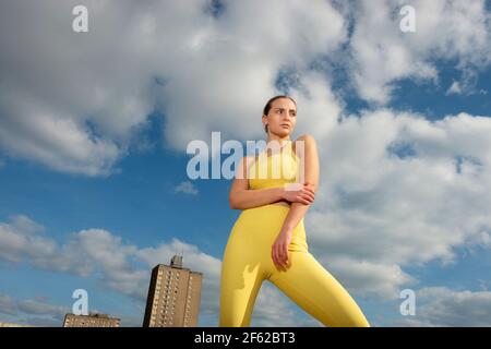 Portrait of young sportswoman wearing yellow activewear against blue sky Stock Photo