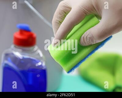 hand in gloves holds sponge over domestic utensils, concept background of household cleaning, close up Stock Photo