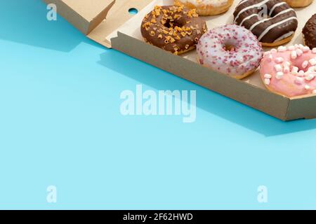 Set of yummy colorful donuts in paper box on blue background. Online delivery take away food Stock Photo