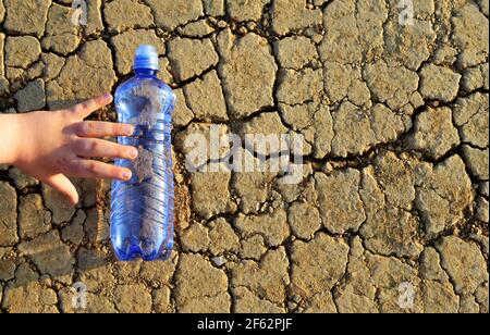 Child's hand reaches a bottle of water lying on dry cracked soil. Concept of the consequences of global warming. Stock Photo