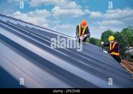 Roofer working in special protective work wear gloves, using air or  pneumatic nail gun installing concrete or CPAC cement roofing tiles on top  of the new roof under construction residential building Stock