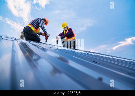 Tow construction worker safety wear using electric drill tools install on new roof metal sheet, Roof construction concept. Stock Photo