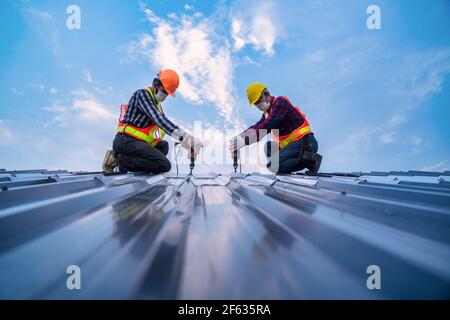 Team work construction worker safety wear using electric drill tools install on new roof metal sheet, Roof construction concept. Stock Photo
