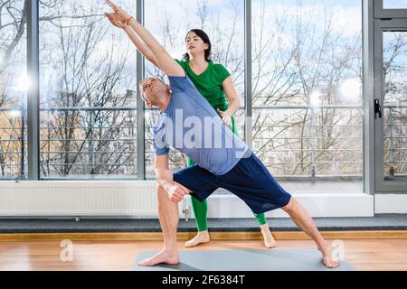 Middle age man stay on mat in light hall with panoramic window and exercise with female doctor, therapeutic gymnastics, health rehabilitation Stock Photo