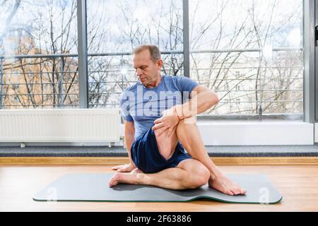 Middle age sportive man during workout training on floor mat in light studio, twirl and stretch body muscles Stock Photo