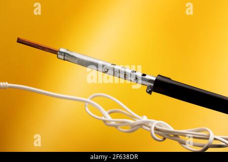 Soldering iron with black plastic handle isolated on yellow background. Tool for soldering and repairing electronic device boards. Stock Photo