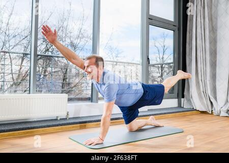 Middle age man stay on floor mat in plank pose, stretch hands and legs at light studio background, healthy workout. Plank with opposite arm and leg li Stock Photo