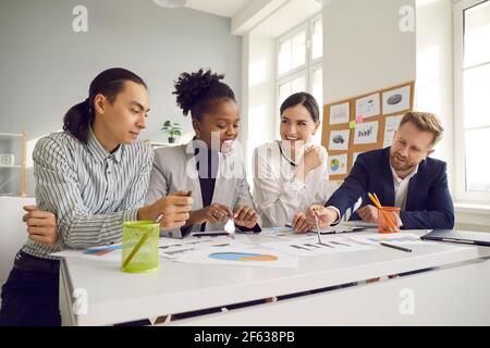 Team of happy entrepreneurs studying paper reports and discussing new business strategy Stock Photo