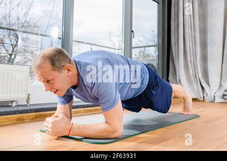 Aged fit sportsman stand in plank yoga fitness pose on floor mat in room, face close up, healthy lifestyle Stock Photo