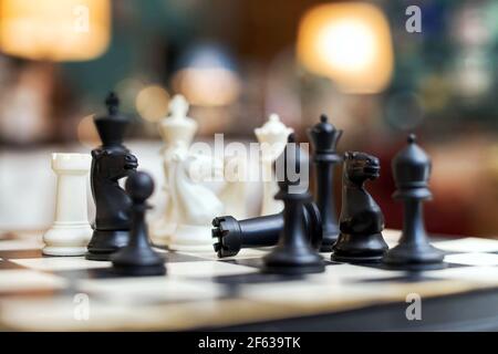 Low angle close up view of a wooden black and white chess set on a chessboard with selective focus to a fallen castle in the centre of the pieces in a Stock Photo