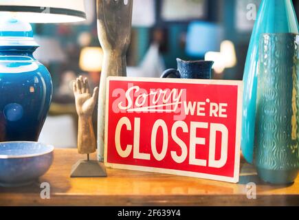 Red notice displayed amongst ceramic handicrafts in a store window - Sorry We're Closed - for business in a concept of after hours trade or lockdown f Stock Photo