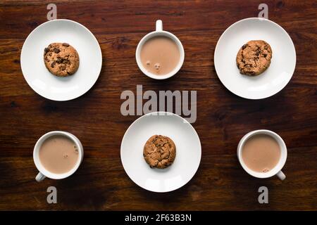 Cookies placed on plates and cups filled with drinking chocolate on wooden desk Stock Photo
