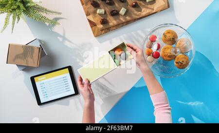 Top view of unrecognizable woman packing biscuits, processing orders desktop concept. Stock Photo