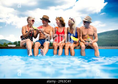 Group of cheerful seniors sitting by swimming pool outdoors in backyard. Stock Photo