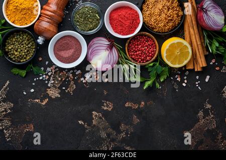 Set of Indian fragrant spices and herbs on a black stone background. Turmeric, dill, paprika, cinnamon, saffron, basil and rosemary in a spoon. Top vi Stock Photo