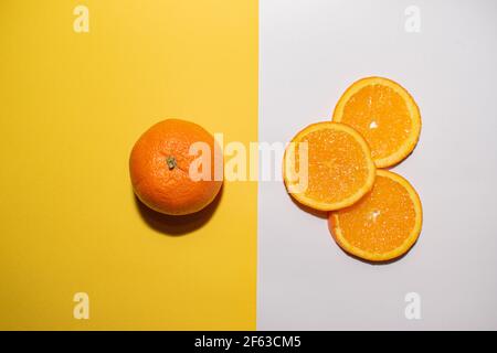 Three orange slices pointing to a whole orange, the image is divided in two by a line separating a yellow background from a white one. Stock Photo