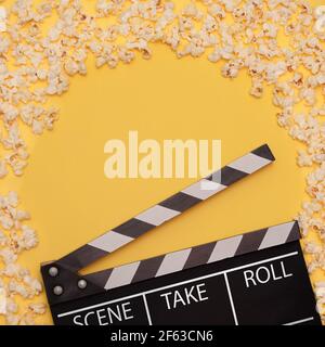 Black and white movie clapperboard on yellow background with freshly popped popcorn surrounding the space and leaving a gap in the center Stock Photo