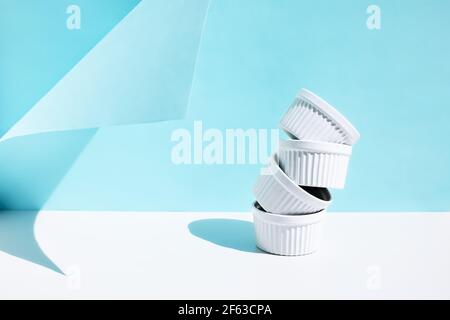 Stack of four white ceramic bowls on blue pastel background with hard shadows. Creative kitchen tableware. Stock Photo
