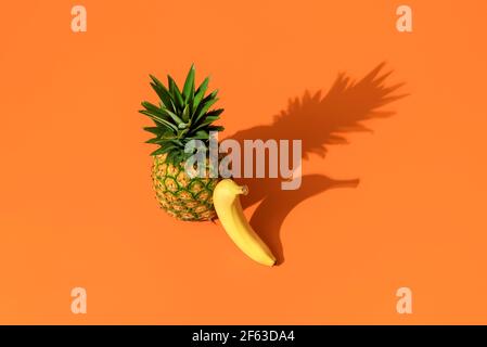 Top view with a pineapple and banana isolated on an orange background. Minimalist shot with two summer fruits in bright light. Stock Photo