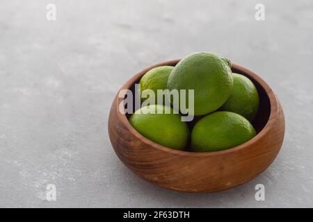 Bright Green Limes in Wooden Bowl on Gray Surface Stock Photo