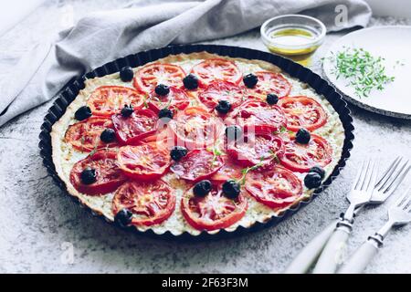 Vegetable tart with tomatoes, ricotta, black olives and thyme on grey background. Vegetarian healthy food concept. Stock Photo
