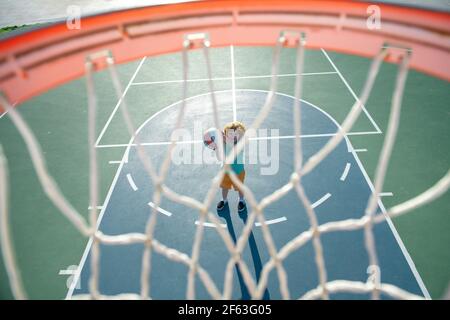 Angle view from on top of basketball basket, selective focus on basketball kid player. Sport texture background. Stock Photo