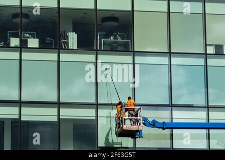 Window cleaners using a cherry picker platform to wash high office windows. Workers using aerial work platform to access tall building. Water fed pole Stock Photo