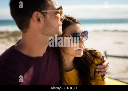 Happy caucasian couple sitting on beach by the sea embracing Stock Photo