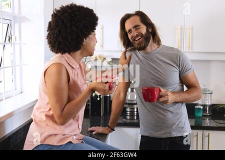 Happy diverse couple in kitchen drinking coffee and smiling Stock Photo