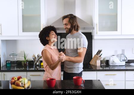 Happy diverse couple dancing in kitchen and smiling Stock Photo