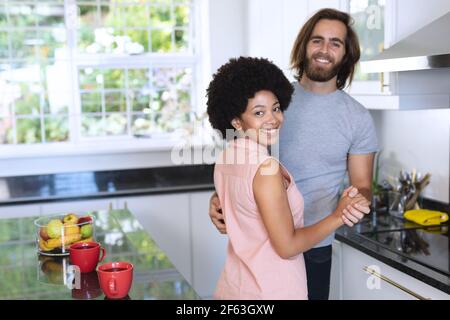 Portrait of happy diverse couple dancing in kitchen and smiling Stock Photo