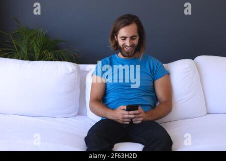 Caucasian man sitting on sofa using smartphone and smiling Stock Photo