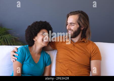 Happy diverse couple sitting on sofa embracing and smiling Stock Photo