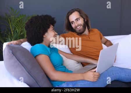 Happy diverse couple sitting on sofa embracing and using laptop Stock Photo