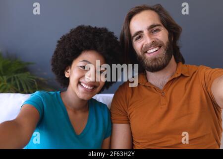 Portrait of happy diverse couple sitting on sofa embracing and smiling Stock Photo