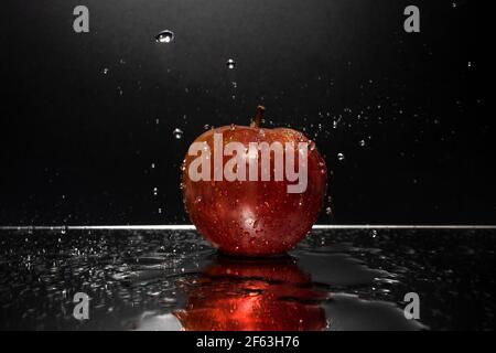 A red apple resting on a mirror with falling water drops Stock Photo