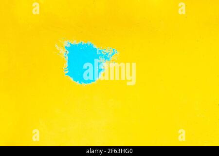 A blue spot of paint on a bright yellow wall. Artwork, urban design art color abstract background. Stock Photo