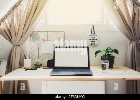 Modern workplace - wooden desk with laptop mockup white empty screen, mood board with pined notes, green plants at work space in home office room Stock Photo