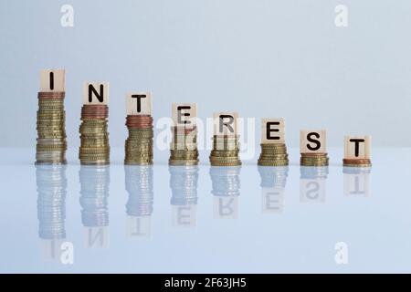 Word 'INTEREST' on wooden blocks on top of descending stacks of coins against gray background. Concept photo of economy, business, finance and banking Stock Photo