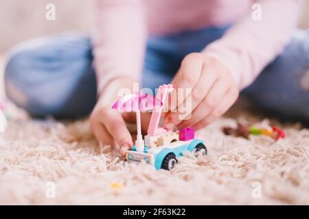 Close up focus view of a plastic toy car with umbrella on the carpet while little girl hands holding it. Stock Photo