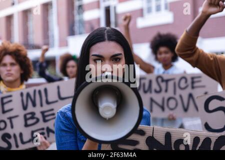 Mixed race woman using megaphone with protesters on march holding protest signs and raising fists Stock Photo