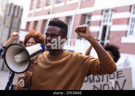 African american man using megaphone with protesters on march holding signs and raising fists Stock Photo