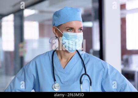 Caucasian female doctor wearing face mask, scrubs and stethoscope looking away Stock Photo