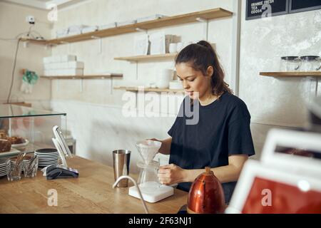 Professional barista preparing coffee using chemex pour over coffee maker and drip kettle. Young woman making coffee. Alternative ways of brewing Stock Photo