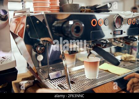 Espresso pouring from coffee machine in cardboard cup. Professional coffee brewing Stock Photo