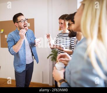 Group of young playful happy coworkers having fun on break while together drinks coffee in the paper cup. Stock Photo