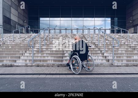 Disabled man in a wheelchair waiting at the bottom of steps. Stock Photo