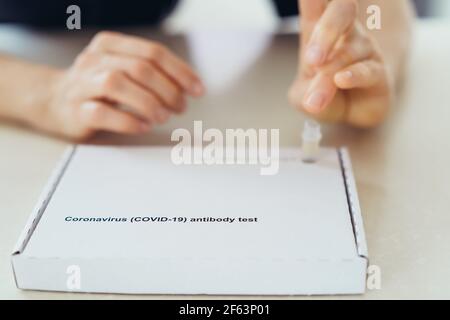 Woman doing herself test for antibodies to coronavirus Covid 19. She pierced her finger and drips blood onto the express test panel for Ig M and Ig G Stock Photo