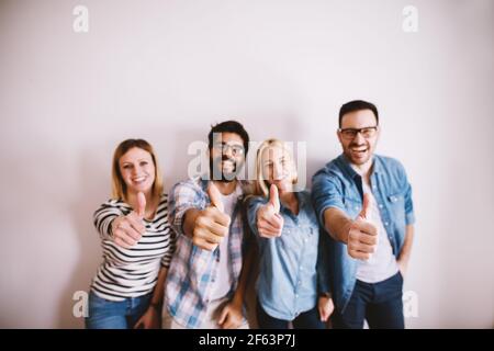 Group of young handsome business colleague people standing against the wall showing with thumbs up and looking at the camera. Stock Photo
